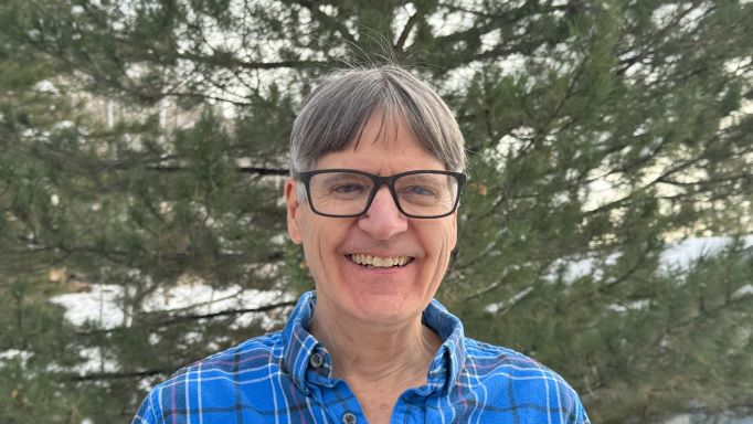 close-up photo of Peter Torpey in front of a large pine tree on a snowy day